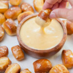 Beer cheese dip in a brown bowl surrounded with soft pretzel bites.