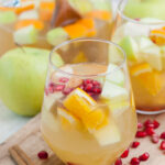 Two glasses with apple cider sangria on a wooden board.