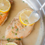 Pan-fried chicken fillet in a frying pan is being poured with lemon butter sauce.