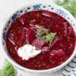 Beet soup in a white-blue plate topped with sour cream and dill.