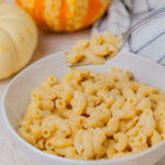 Pumpkin mac and cheese in a white bowl. Small pumpkins in the background.