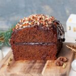 Piernik cake cut in half on a wooden board. Christmas decorations in the background.