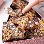 A child's hand is reaching for pretzel toffee in a cookie tin.