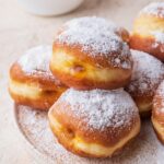 Krapfen dusted with powdered sugar on a white plate.