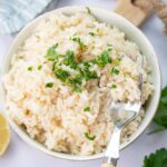 Garlic butter rice in a white bowl topped with chopped parsley with a fork on the side.