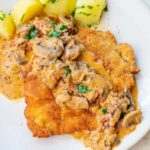 Jägerschnitzel with mushroom sauce served with potatoes on a beige plate.