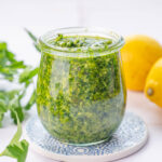 Parsley pesto in a jar. Parsley leaves and lemons in the background.