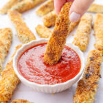 Zucchini fry is being dipped in marinara sauce.