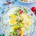 Chlodnik ogorkowy soup in a white bowl topped with eggs, potatoes, and radishes.