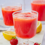 Two glasses with strawberry lemonade on a marble board.