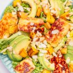 Halloumi salad with pineapple and avocado on a blue plate.