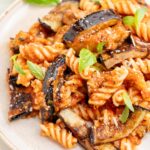 Pasta alla Norma on a white plate sprinkled with basil and parmesan.