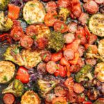 Roasted sausage slices and chopped vegetables on a baking sheet.