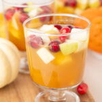 Two glasses with Thanksgiving sangria on a wooden board. Mini pumpkins and cranberries in the background.