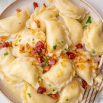 Pierogi ruskie topped with bacon and onions on a beige plate.