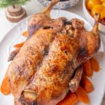 Danish Christmas Duck on a white plate with caramel potatoes and red cabbage in the background.